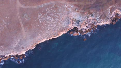 Top-down-aerial-view-of-waves-splash-against-rocky-seashore,-background