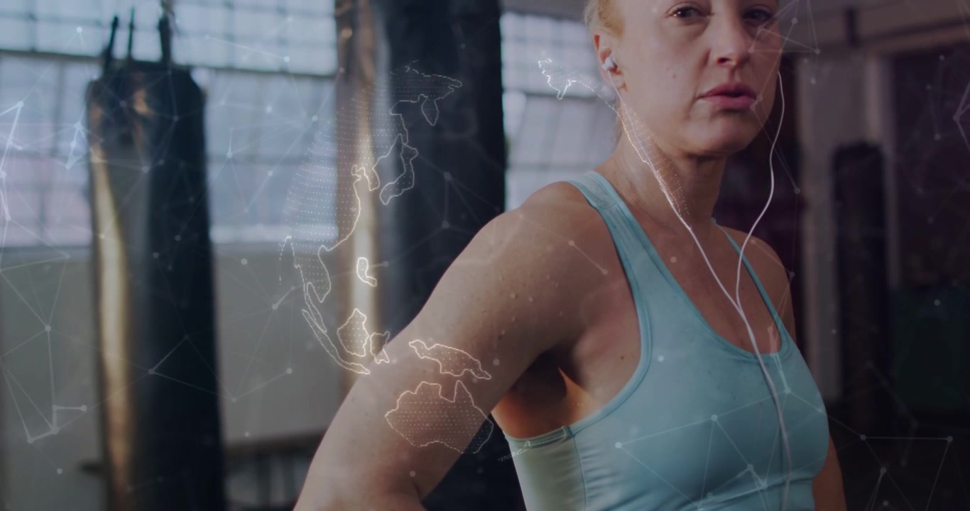 Vertical video: Overlay appearing, woman in bra with wired earbuds prepping near heavy bags in gym