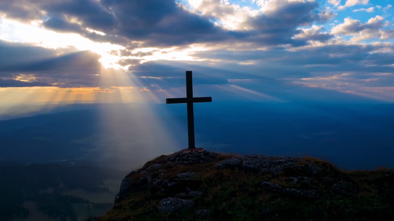 Video aéreo que captura una cruz en una montaña al atardecer, con dramáticos rayos de luz irrumpiendo