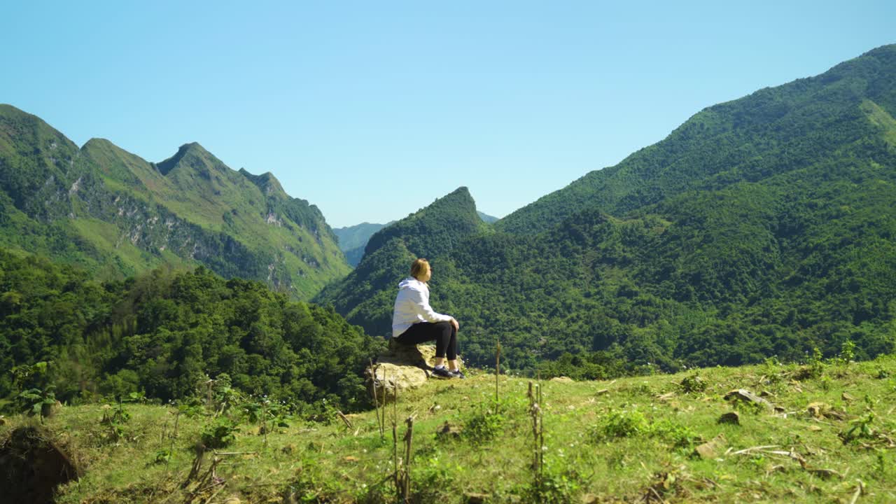 젊은 활발한 여성 하이커를 따라 산꼭대기에 도달하여 앉아서 파노라마 전망을 바라보고 있습니다.
