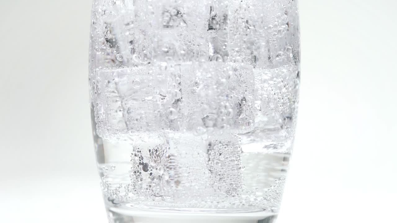느린 동작으로 유리를 채우는 얼음 조각에 탄산수나 탄산수를 붓고 탄산 흰색 스튜디오 배경을 닫습니다.