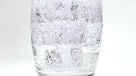 soda o agua con gas que se vierte en cubitos de hielo que llenan el vaso en burbujas de cámara lenta cierran el fondo blanco del estudio de carbonatación