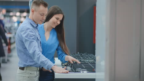 Una-Pareja-Joven-Elige-Una-Placa-De-Cocina-En-Una-Tienda-De-Electrodomésticos.