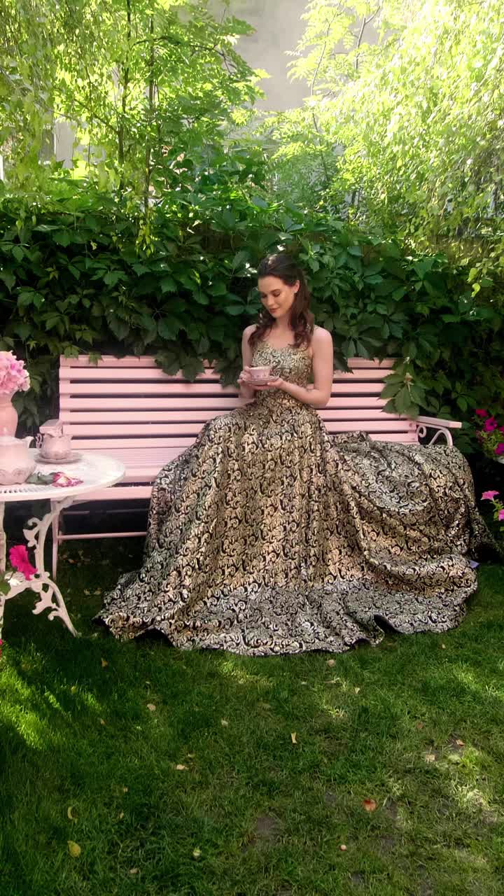 Woman in a Golden Dress Having Tea in a Garden