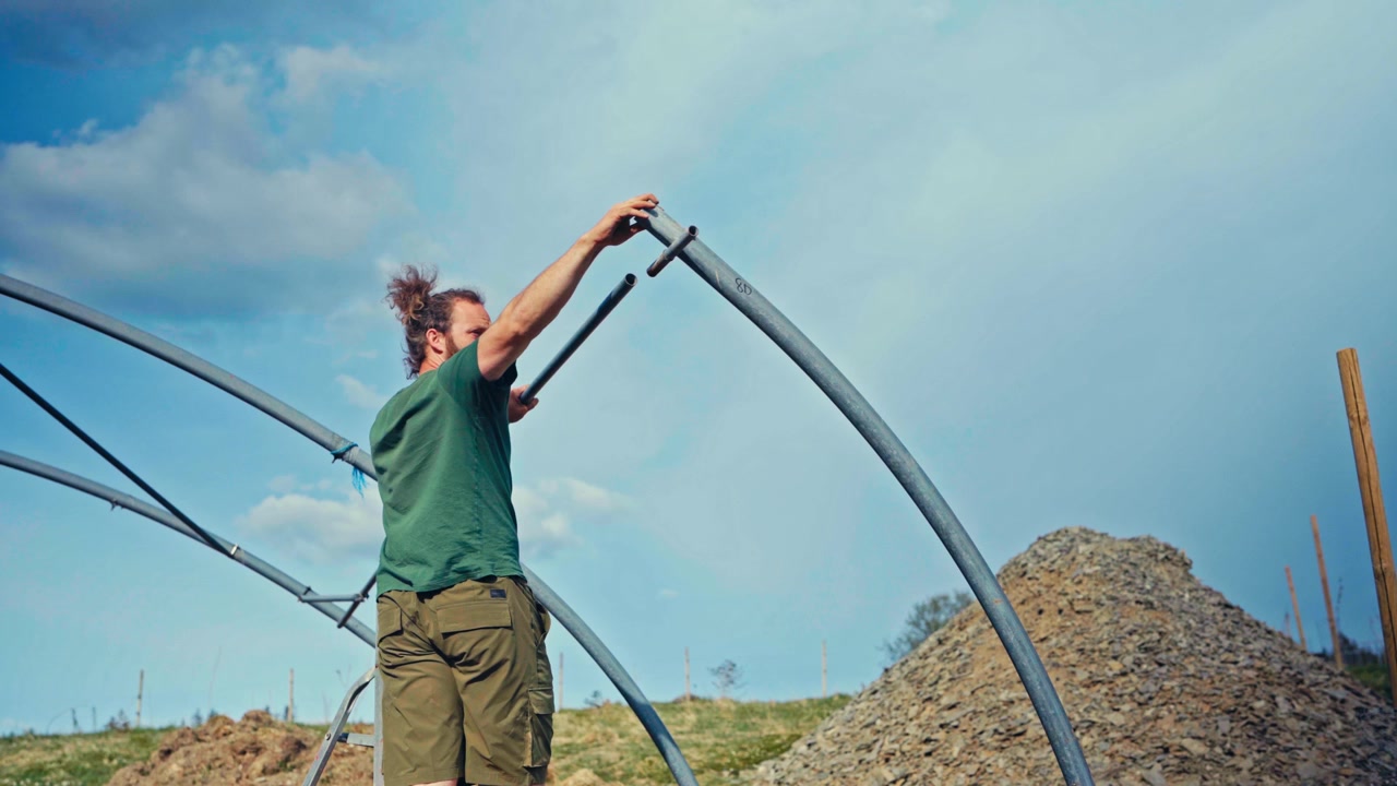 Uomo che costruisce una serra a tunnel su un terreno agricolo rurale in Norvegia, assembla la struttura per uso agricolo e da giardinaggio.