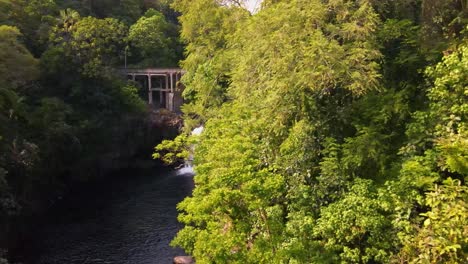 Enchanting-drone-reveal-capturing-a-bridge-gracefully-spanning-over-a-cascading-waterfall-in-the-heart-of-a-lush-rainforest-on-Big-Island,-Hawaii