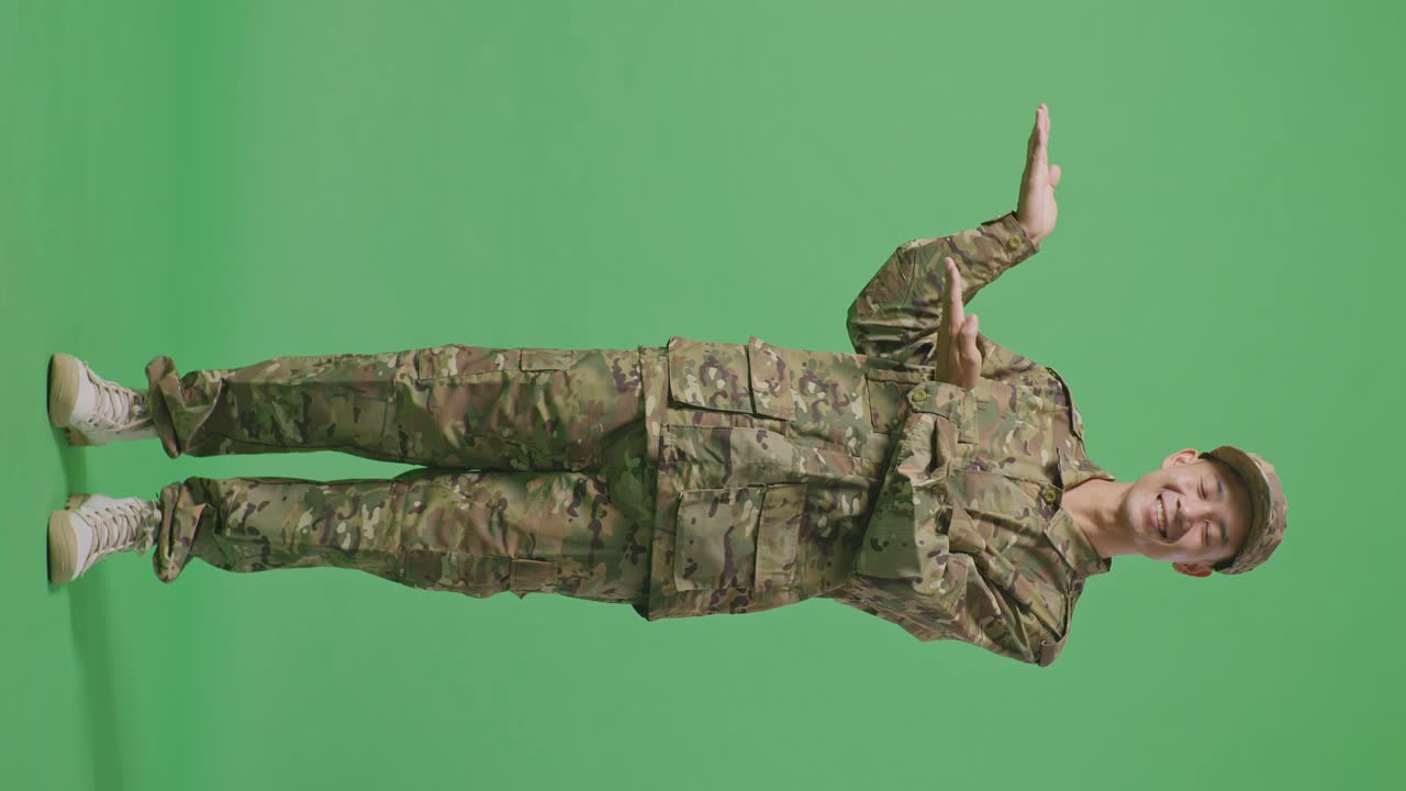 Full Body Of Asian Man Soldier Smiling And Pointing To Side While Standing In The Green Screen Background Studio
