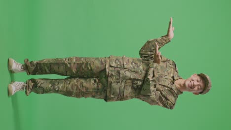 full body of asian man soldier smiling and pointing to side while standing in the green screen background studio