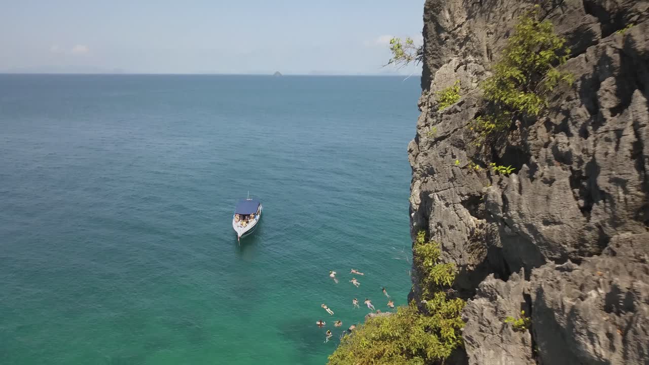 Touristic Boats and Tourist Snorkeling In Tropical Sea By Picturesque Island Cliff, Tilt Down Aerial