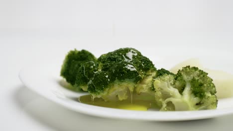 Close-up-Pour-Olive-Oil-on-cooked-broccoli-on-white-plate,-Slow-motion-shot