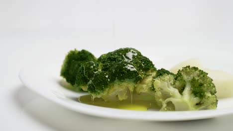 close-up pour olive oil on cooked broccoli on white plate, slow motion shot