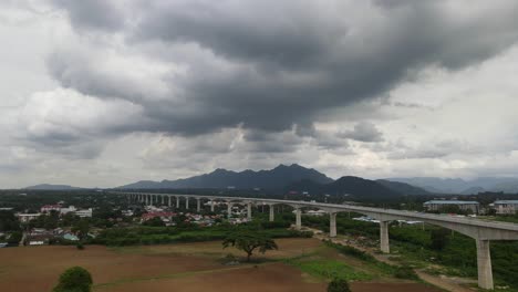 4K-Aerial-descending-shot-showcasing-Muak-Lek-mountainous-silhouette-of-a-gloomy-thunderous-weather-with-futuristic-elevated-railway-across-the-frame-in-Saraburi,-Thailand