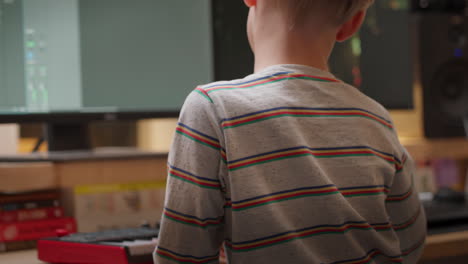 A-young-boy-at-a-desk-in-a-home-studio-uses-a-keyboard-and-dual-monitors-to-create-electronic-music