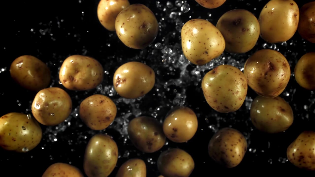 Rallentatore di patate fresche e gocce d'acqua su sfondo nero