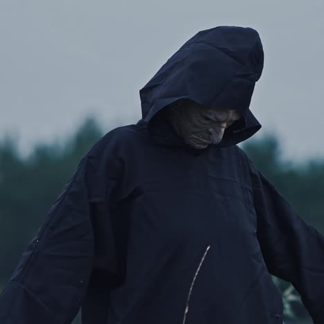 mysterious dark demon outdoors. scary face of ghost evil in black costume with hood on blur trees background. halloween concept.