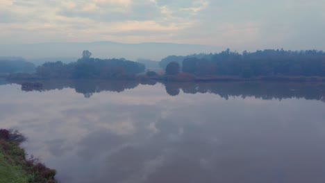 panning shot of a beautiful reflective lake in the slovenian countryside on a foggy autumn morning