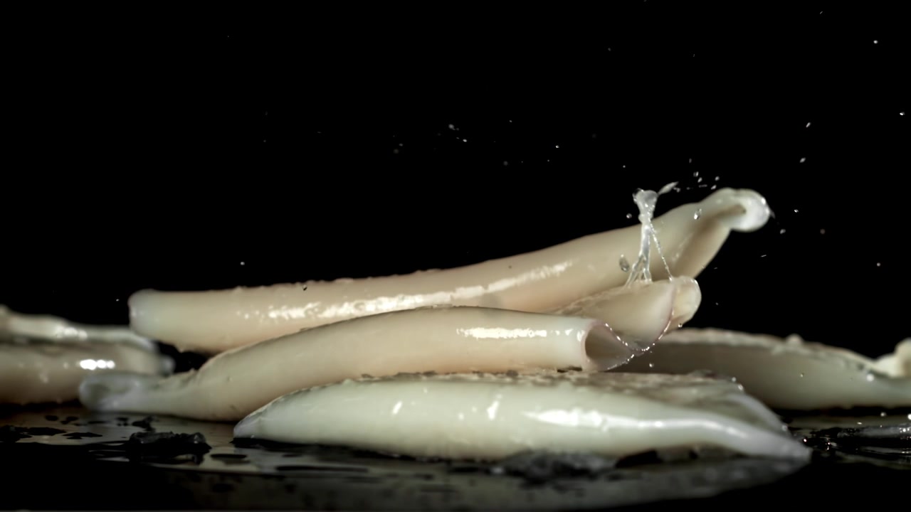 Pezzi di calamaro crudo che cadono e schizzano su sfondo nero