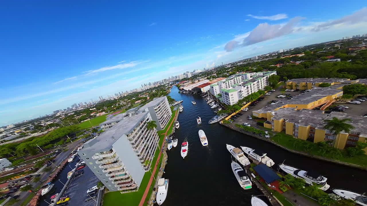 Narrow ricer crosses the cityscape of American city. Multiple yachts and boats are on the water. FPV drone flies above the waterscape.