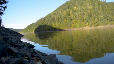 idyllic view of a big lake with reflection on the water and hills in the background in autumn