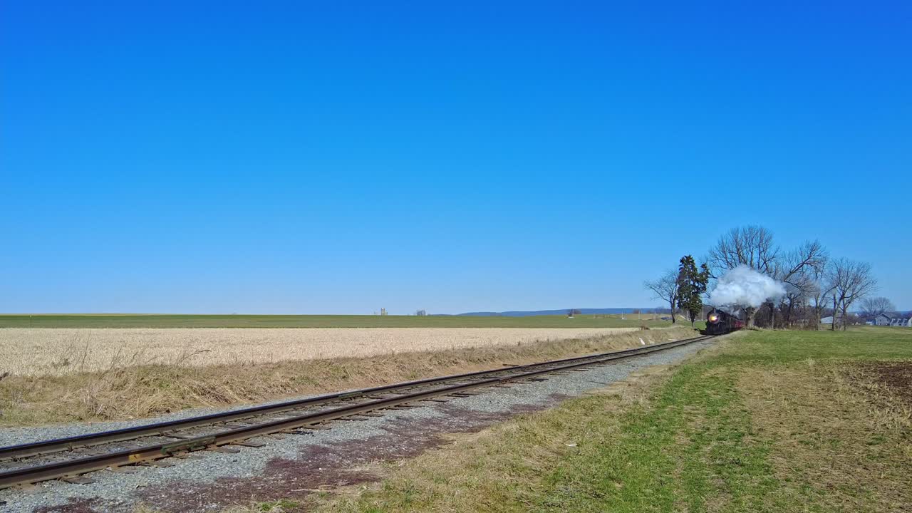 приближающийся паровой пассажирский поезд, выпускающий дым и пар в солнечный день