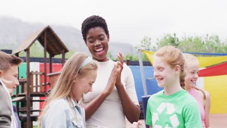 diverse female teacher and happy schoolchildren cleaning together with bags at school playground