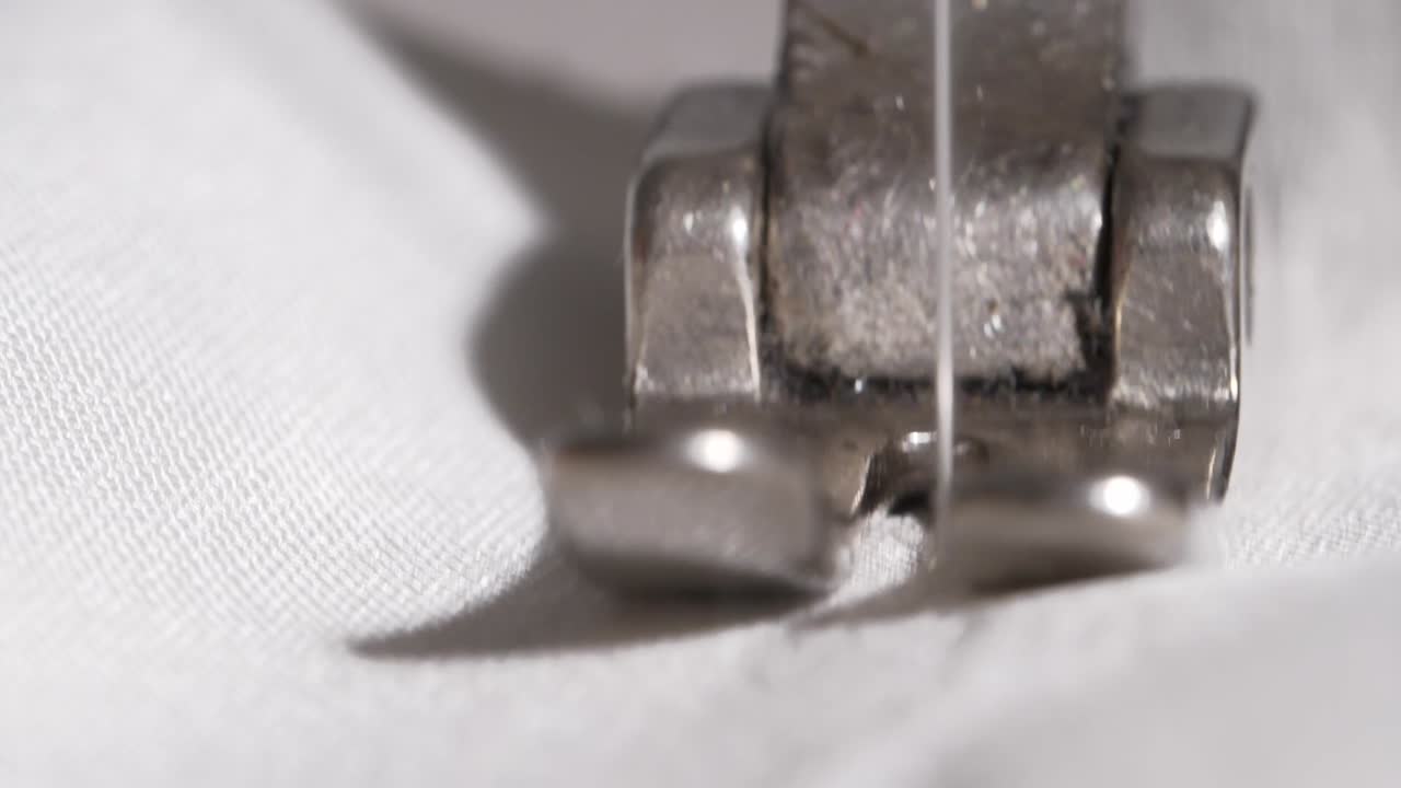 detalle de cámara lenta macro toma de una aguja de máquina de coser penetrando tela blanca con hilo blanco fino