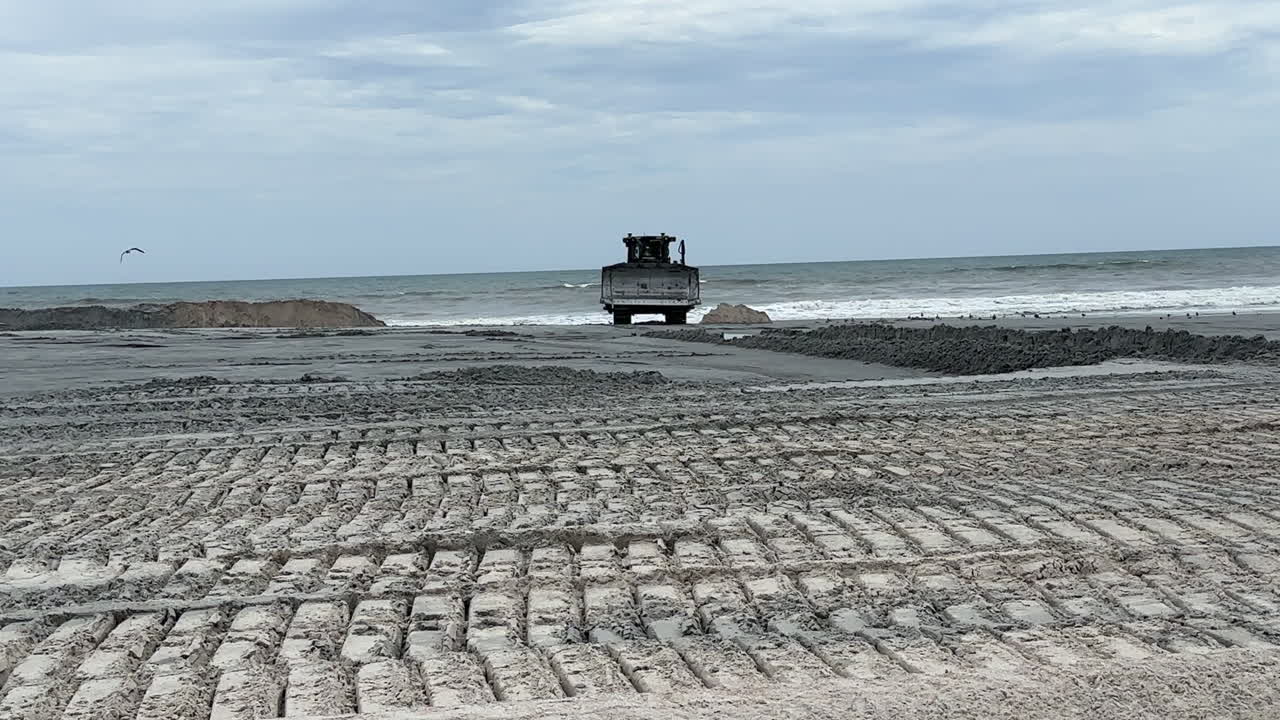 Bulldozer parked on beach near ocean waves, sand replenishment