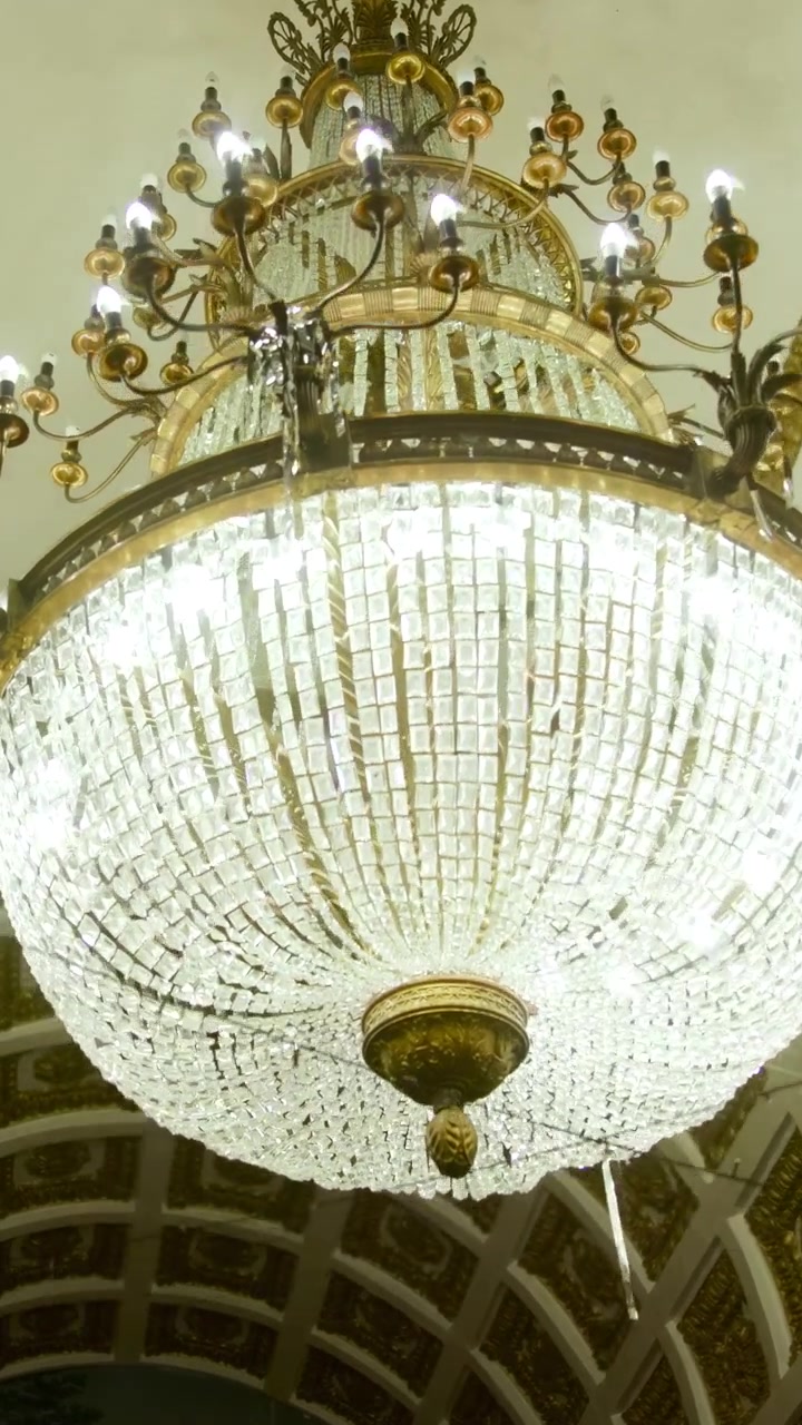 Crystal Chandelier Under Ornate Gilded Ceiling In Historic Ballroom Setting, Glowing Crystal Strands And Brass