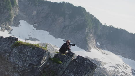 photographer looks through camera viewfinder with telephoto lens on mountain ridge, tim durkan wide tracking helicopter counterclockwise orbit slow motion