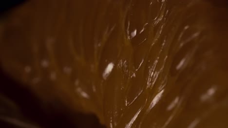 close-up macro shot of a fresh mandarin orange segment with a moving light source reflecting off its juicy surface. the scene is minimalist with very shallow depth of field and a cinematic atmosphere