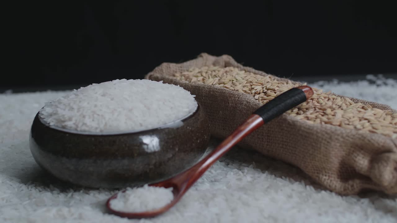 Raw Rice Grain In Unique Bowl, Rustic Bag And Wooden Spoon Rotate In Slow Motion. Pile Of Cereal Long Seeds Rice Close Up