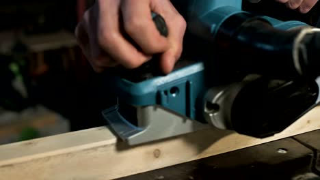 close-up of a carpenter's hand working with an electric plane in a home workshop