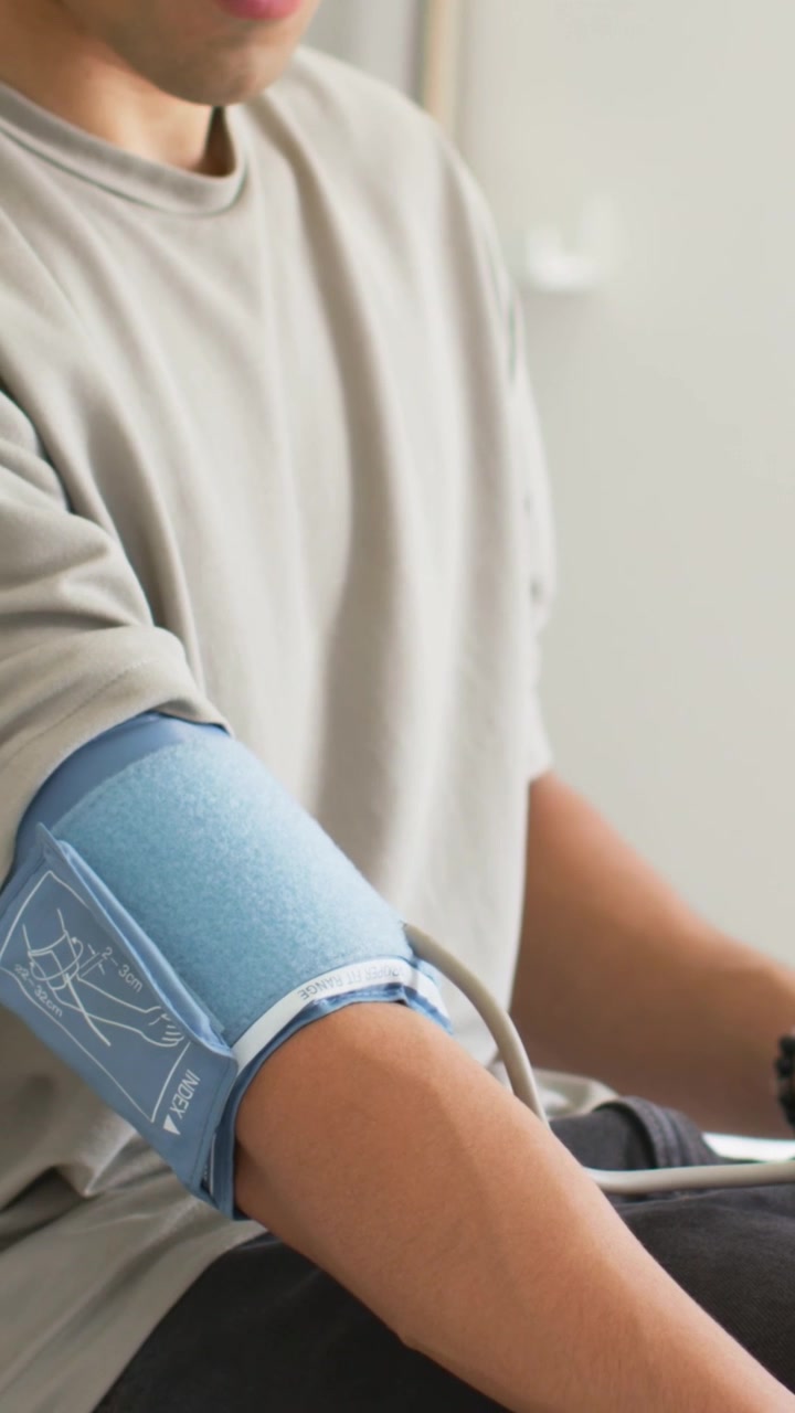 Video verticale: Uomo che si prepara e sistema un bracciale blu sul braccio sinistro a casa, per un controllo della pressione sanguigna.