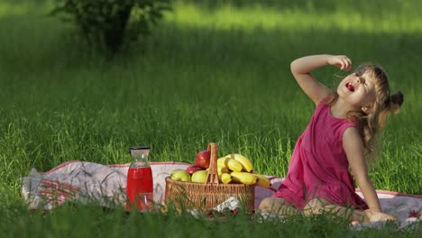 en un picnic de fin de semana, una encantadora niña caucásica en un prado de hierba verde comiendo cerezas.