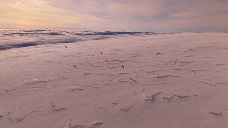 gorgeous aerial drone footage view of people flying kites and surfing with them in norway varanger arctic kite enduro competition during a beautiful sunny winter day. the kite surfing creates shadows.