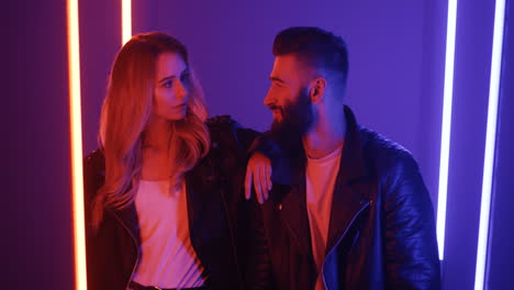 happy young man and woman looking at each other and smiling to the camera on purple neon lights background