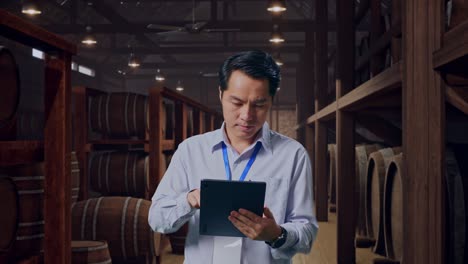 asian male professional worker standing with his tablet in cellar of winery, work continuously with his tablet
