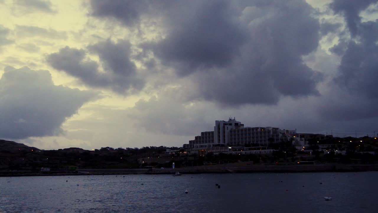 temprano en la mañana en qawra, malta, antes del amanecer, nubes tormentosas lluviosas sobre edificios y tráfico temprano en la mañana