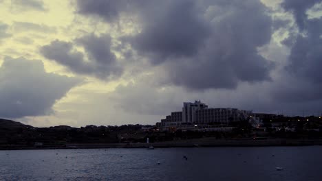 Temprano-En-La-Mañana-En-Qawra,-Malta,-Antes-Del-Amanecer,-Nubes-Tormentosas-Lluviosas-Sobre-Edificios-Y-Tráfico-Temprano-En-La-Mañana