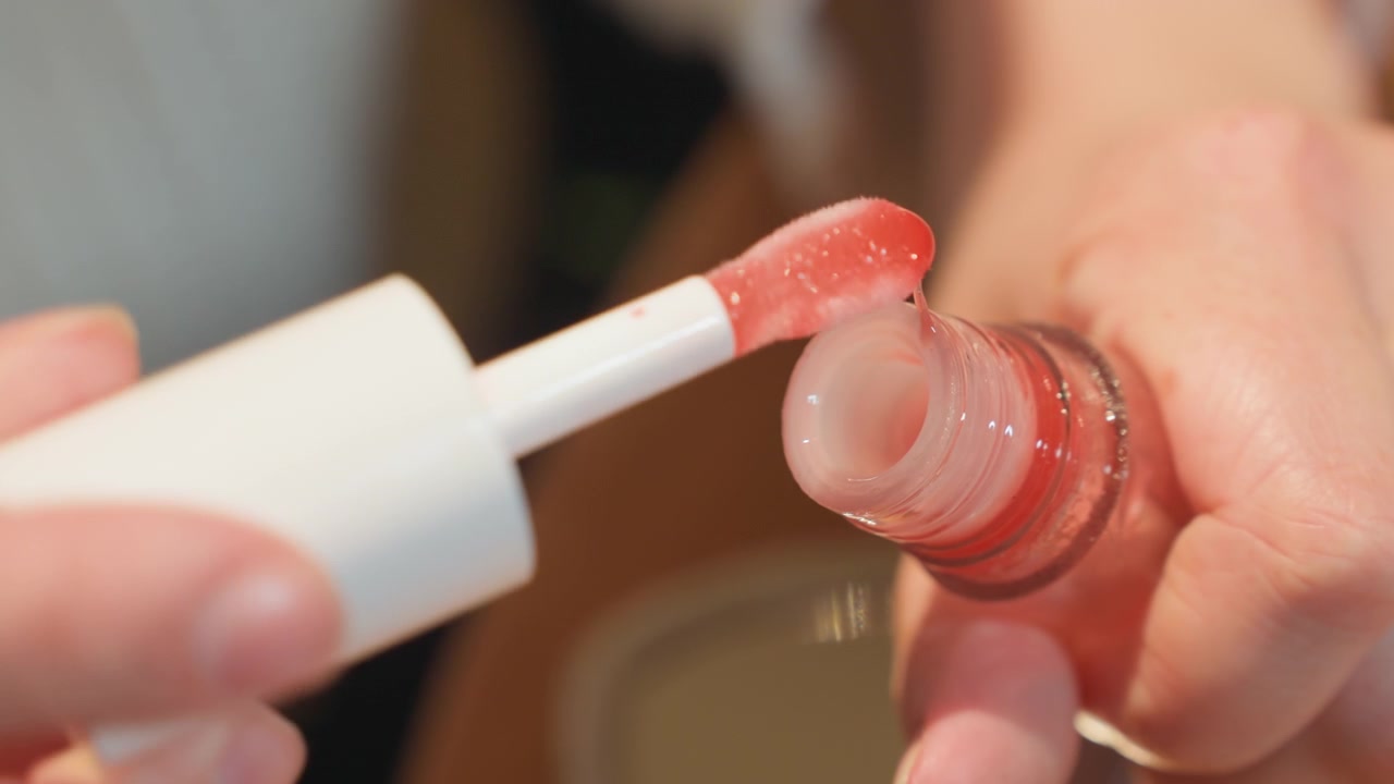 Nærbillede af hænder, der åbner en rød lipgloss-flaske