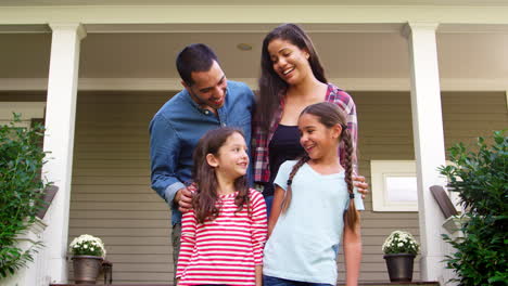 retrato de una familia sonriente de pie frente a su casa