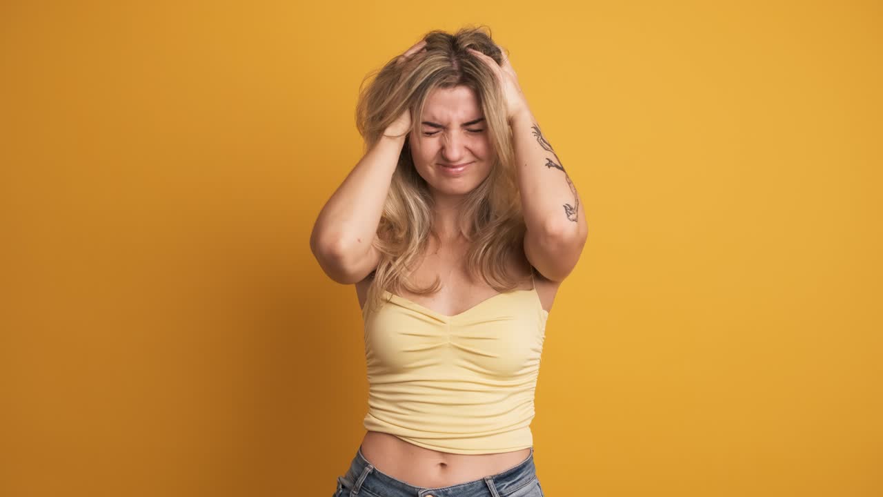 Sad young woman holding head in pain on yellow background