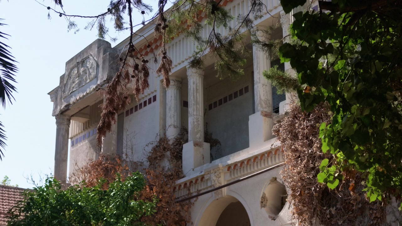 Facciata di villa neoclassica invecchiata con colonne e un frontone scolpito, vista attraverso rami di pino, Costa Azzurra, Francia