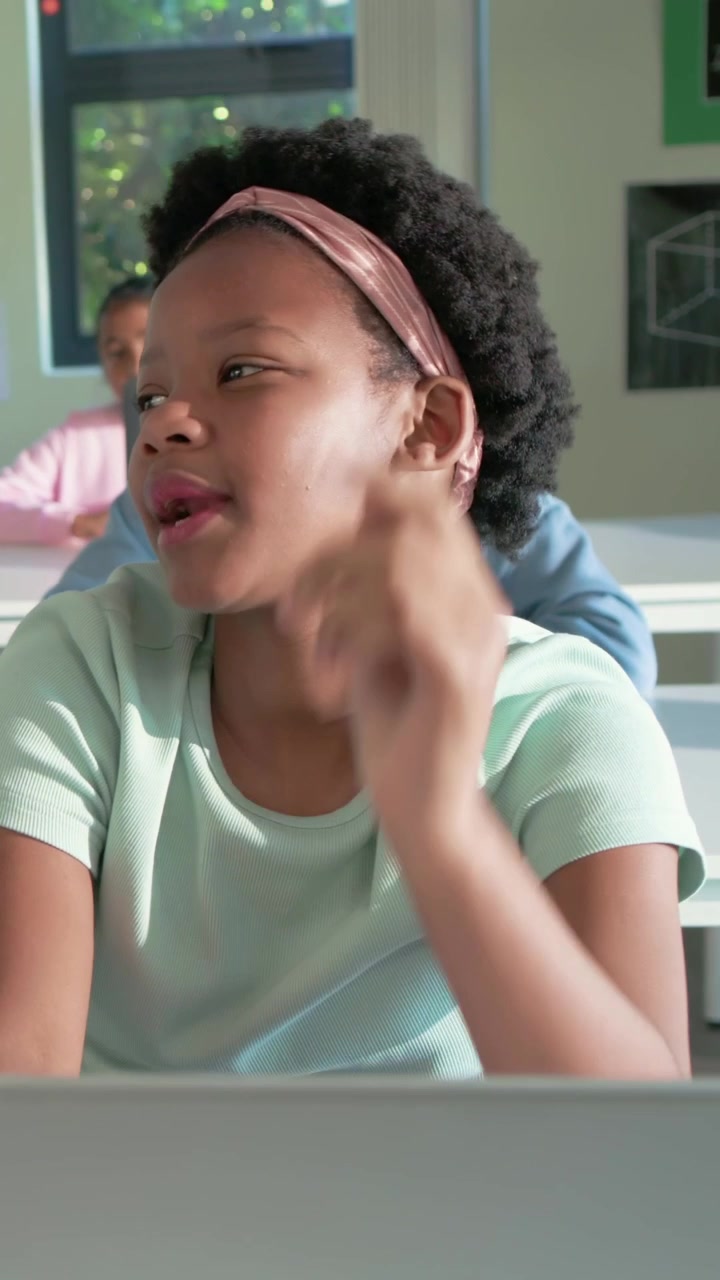 Vertical video: Reacting to teacher call in classroom, pupil in pink headband speaking with laptop