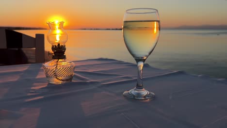 vintage table oil lamp and glass of wine against sunset backdrop