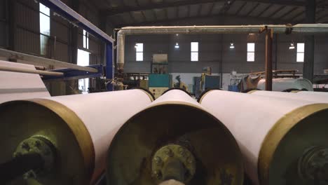 rows of large spinning rollers with white textile fabric inside factory