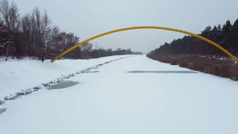 drone video of going under a yellow bridge on top of frozen river in forest in warsaw