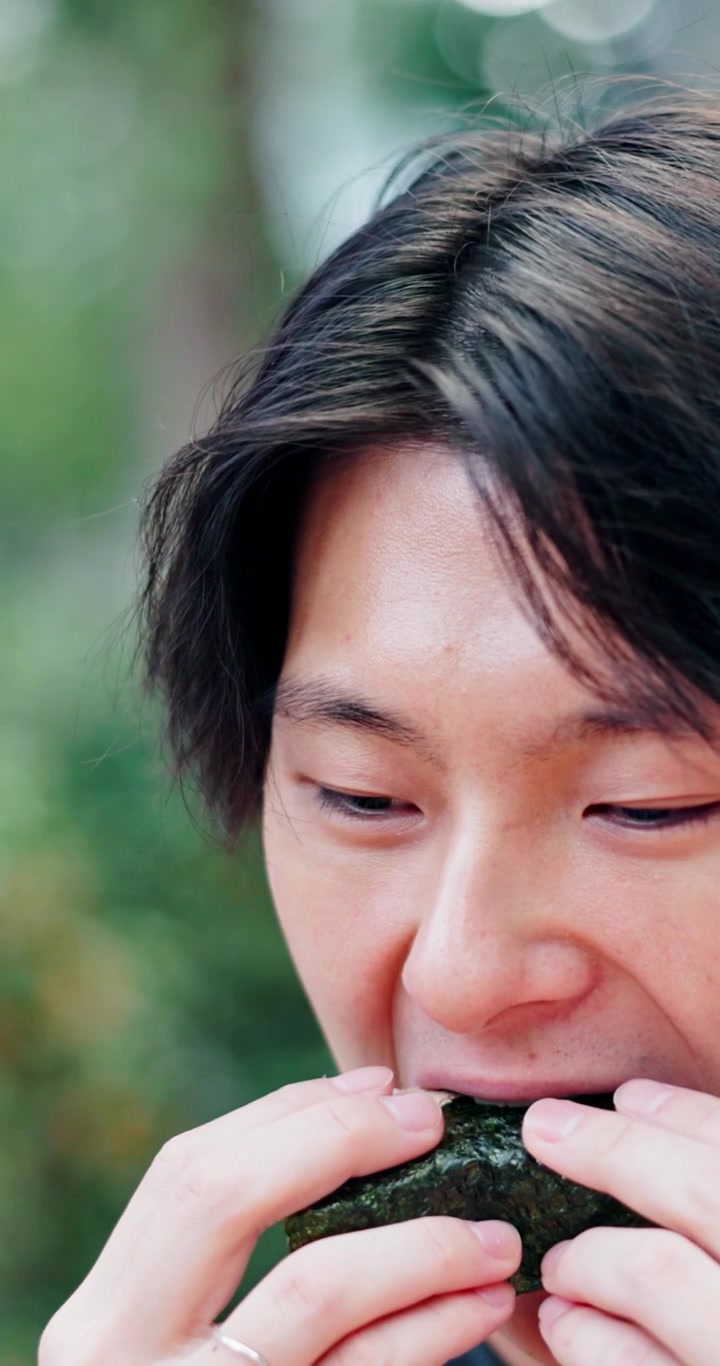 屋外でおにぎりを食べている若い男性