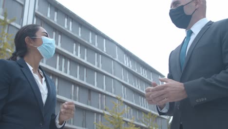 felices colegas de negocios con máscaras faciales reunidas en el edificio de oficinas, saludándose con golpes en los codos y hablando