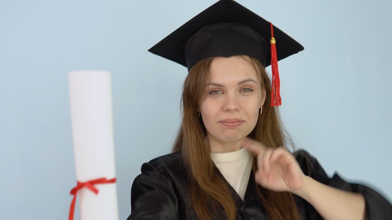 Young caucasian female student in a black gown and master's hat holds in her hands in an upright position a diploma of higher education. A university graduate dances with a diploma . White background